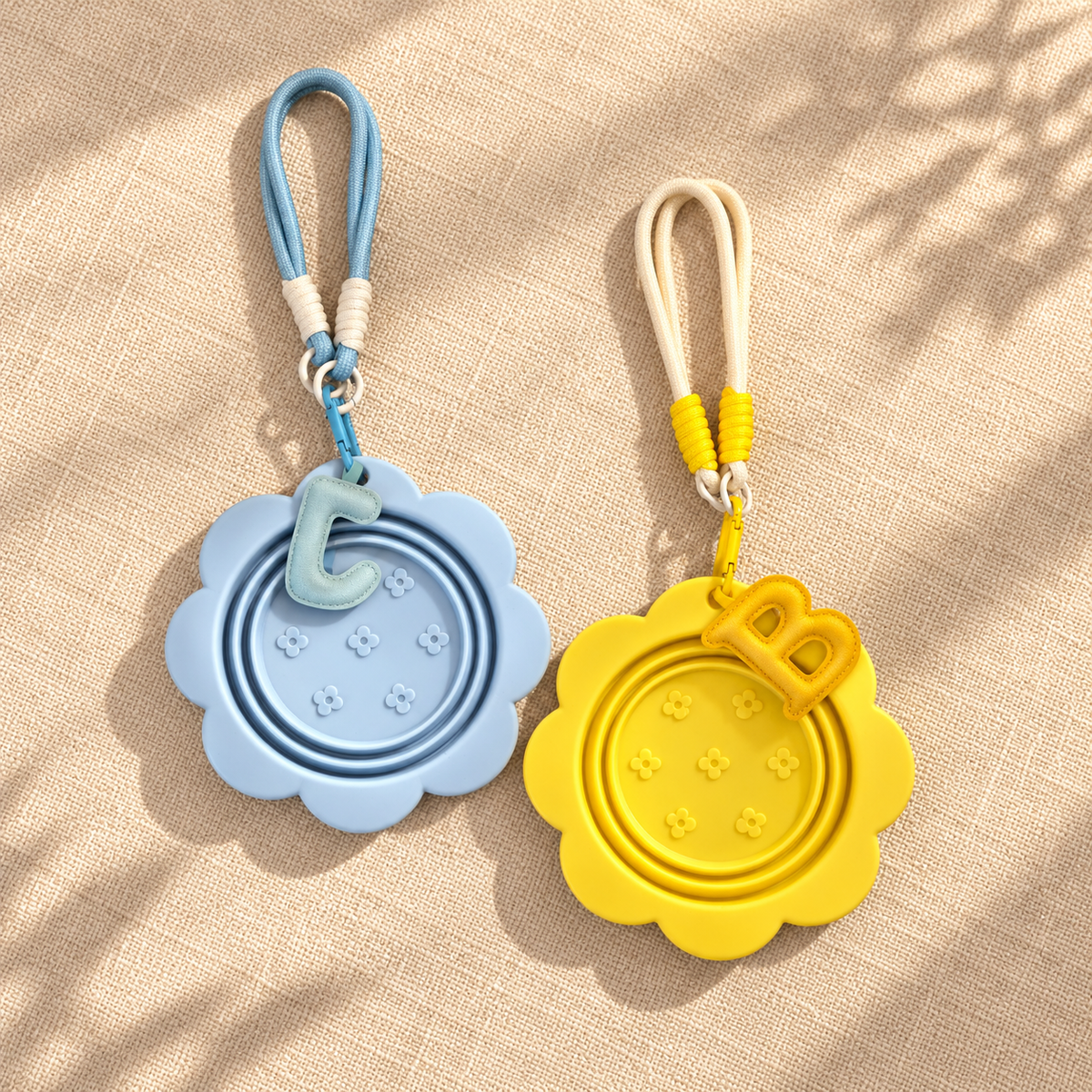 Folded blue and yellow pet travel bowls with matching lanyards, hooks, and letter charms