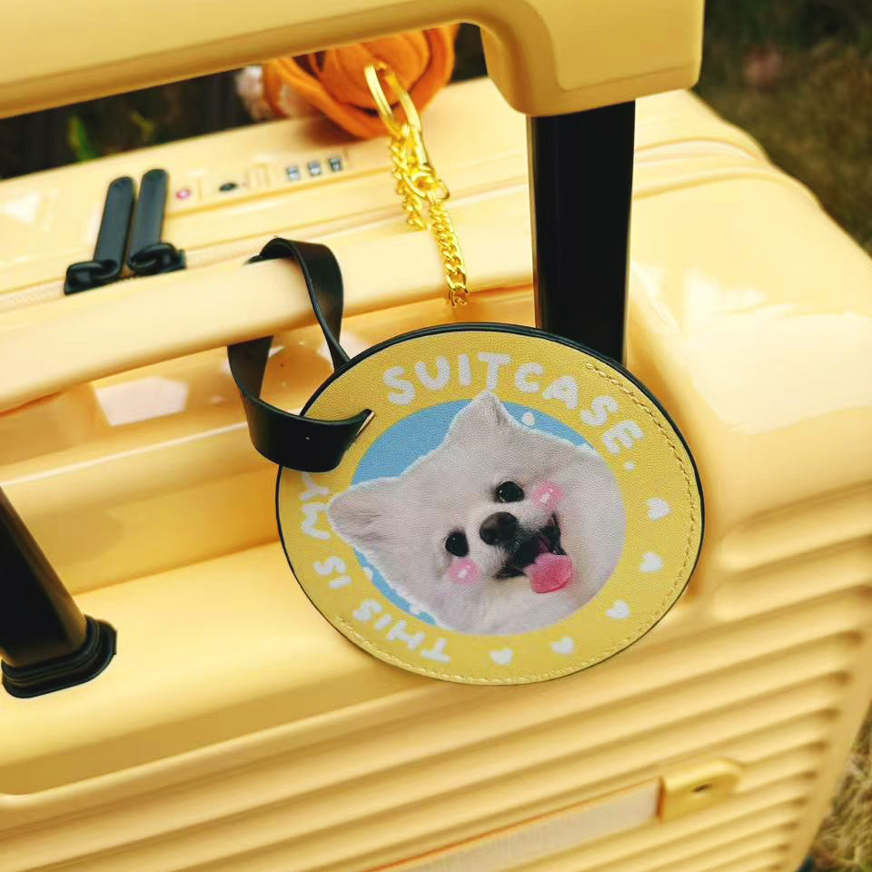 Personalized yellow round pet luggage tag attached to a suitcase handle